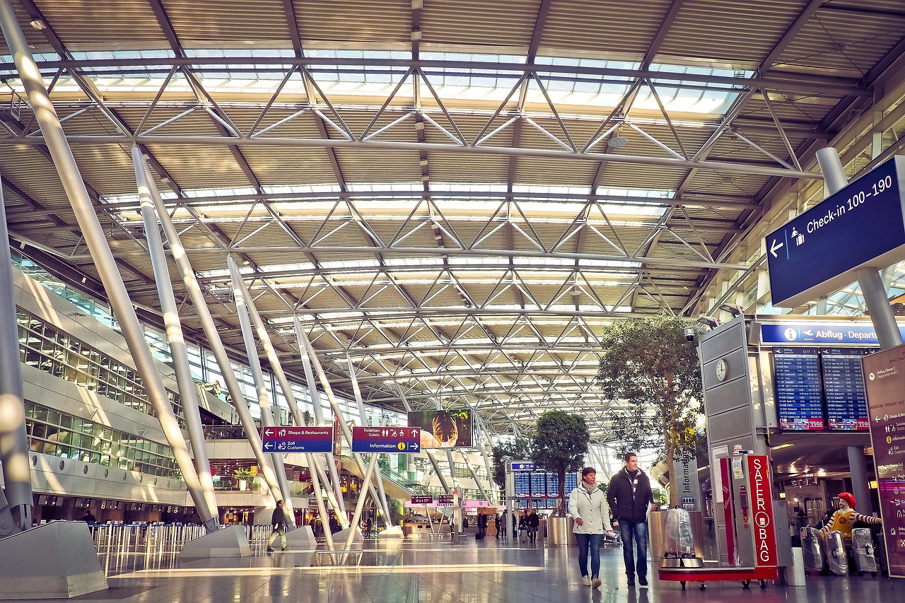Canada eTA and travel insurance: a wide airport terminal with steel roof beams, sunlight, and two travellers walking past a check-in sign