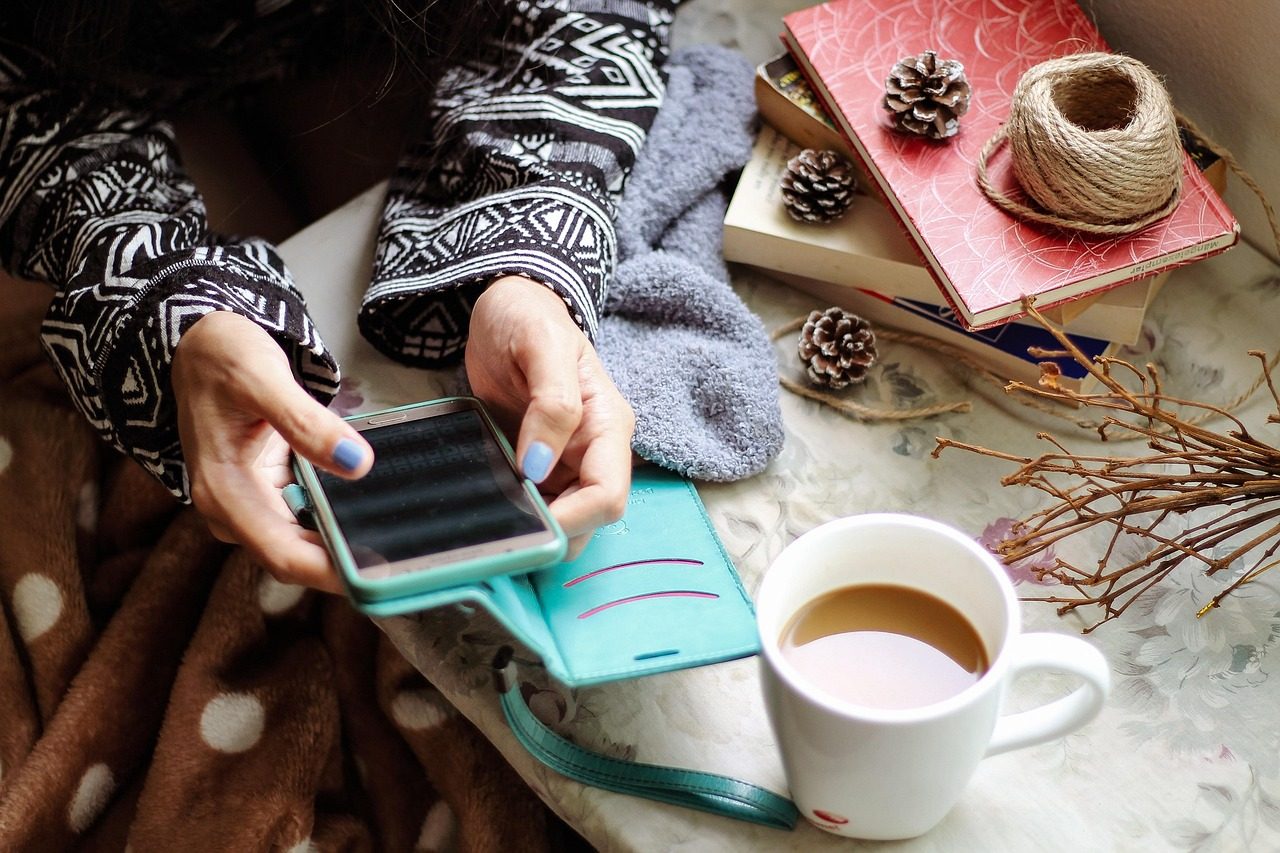 Canada eTA on your phone or computer: hands holding a phone beside a mug of coffee on a cosy table
