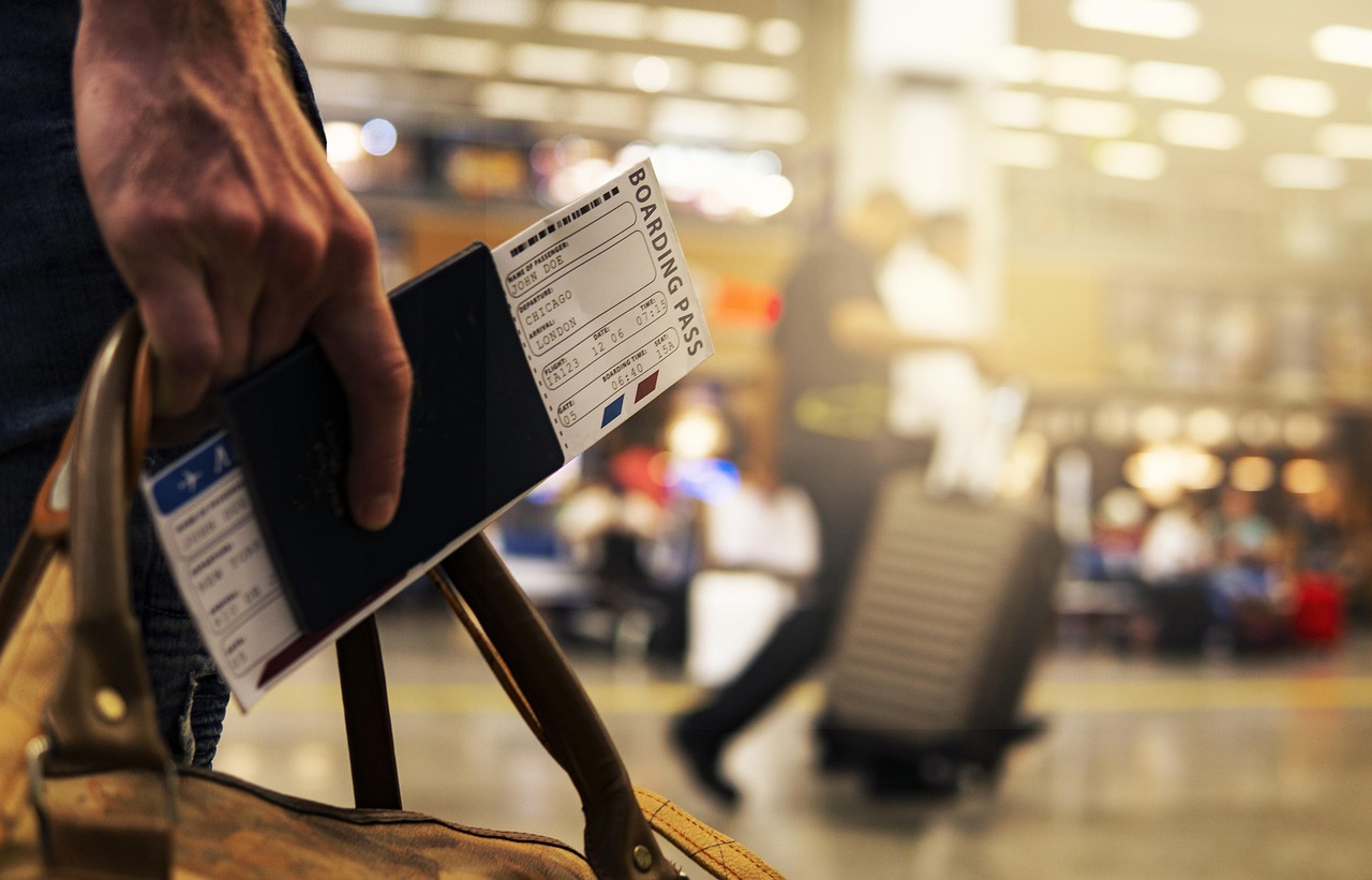 A person’s hand holds a passport and a boarding pass in an airport setting.