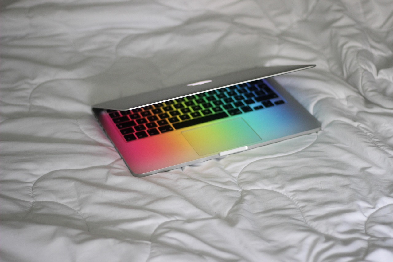 A silver laptop with a colorful screen and keyboard, fully open on a white quilted surface.
