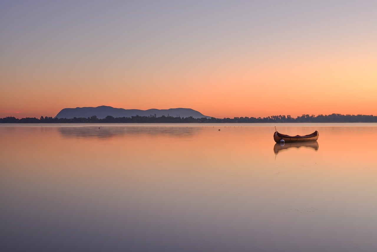 Seasonal work in Canada and the eTA: a lone wooden canoe on a still lake at sunrise, orange sky behind