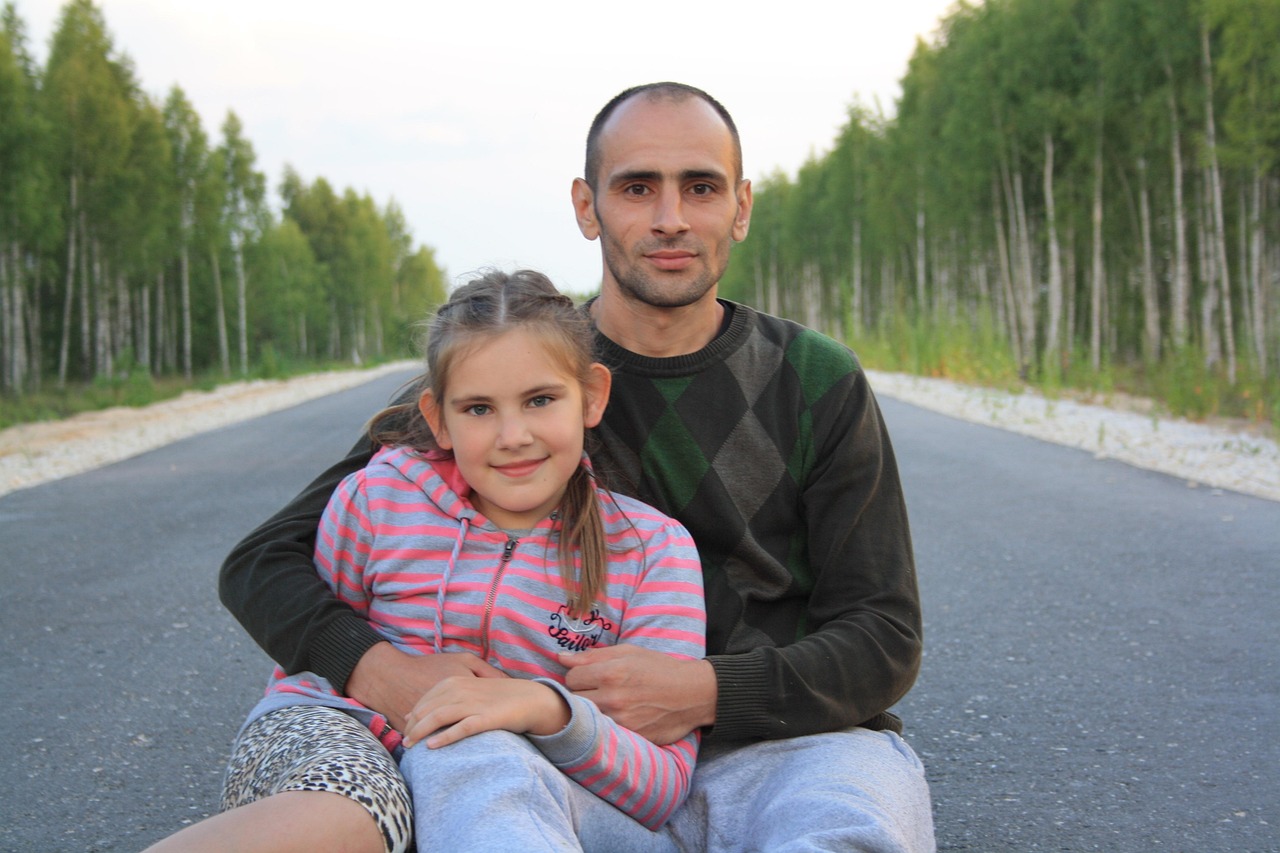 Canada eTA for Visiting Family and Friends: a father and daughter sitting together on a path lined with birch trees, posing for the camera