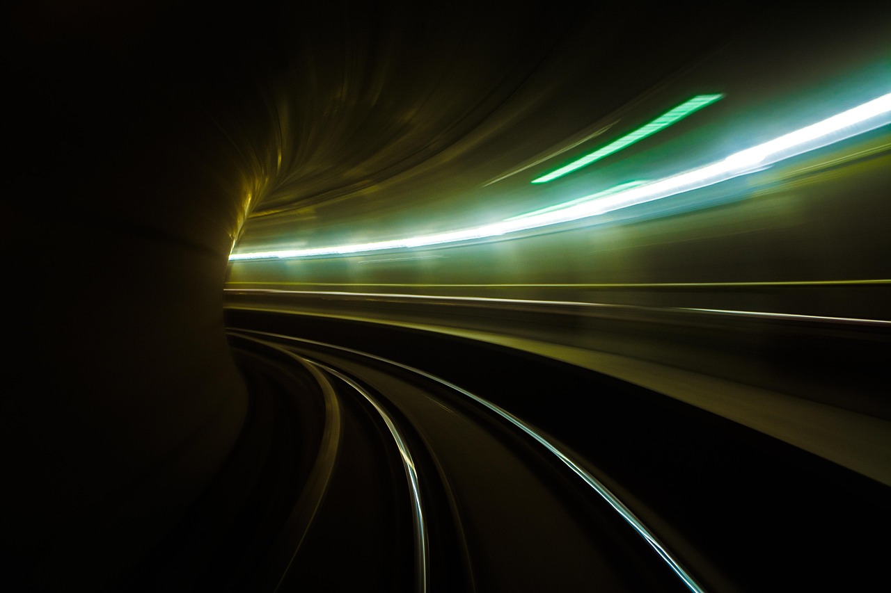 Long exposure of train tracks curving inside a dark tunnel with green and white light streaks.