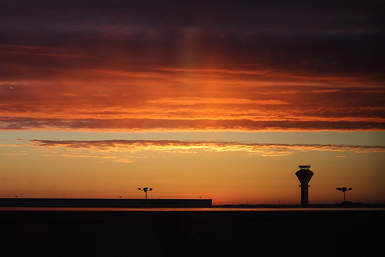 Silhouette of an airport control tower and structures against a vibrant orange and red sunset sky.